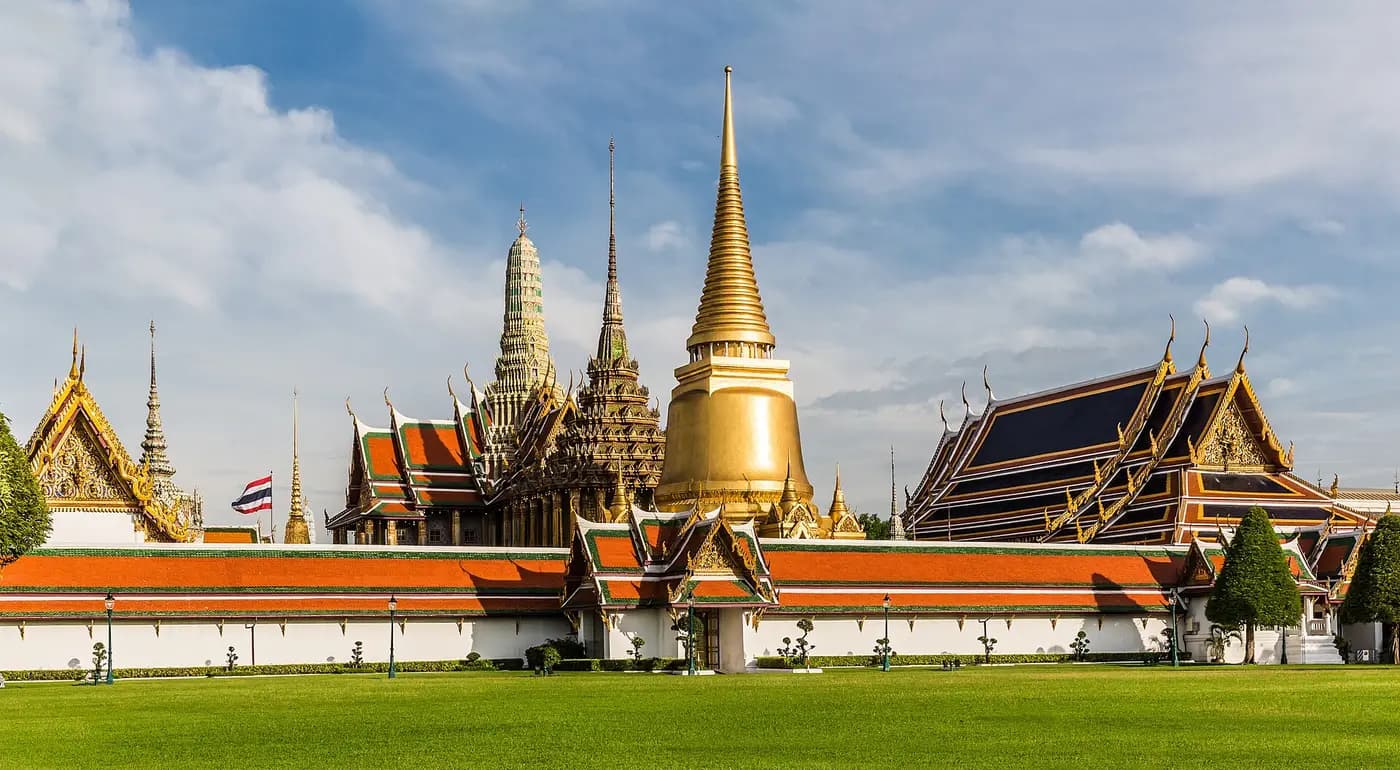 Gilded chedi and tiered temple roofs of Wat Phra Kaew rising above the Grand Palace walls in Bangkok