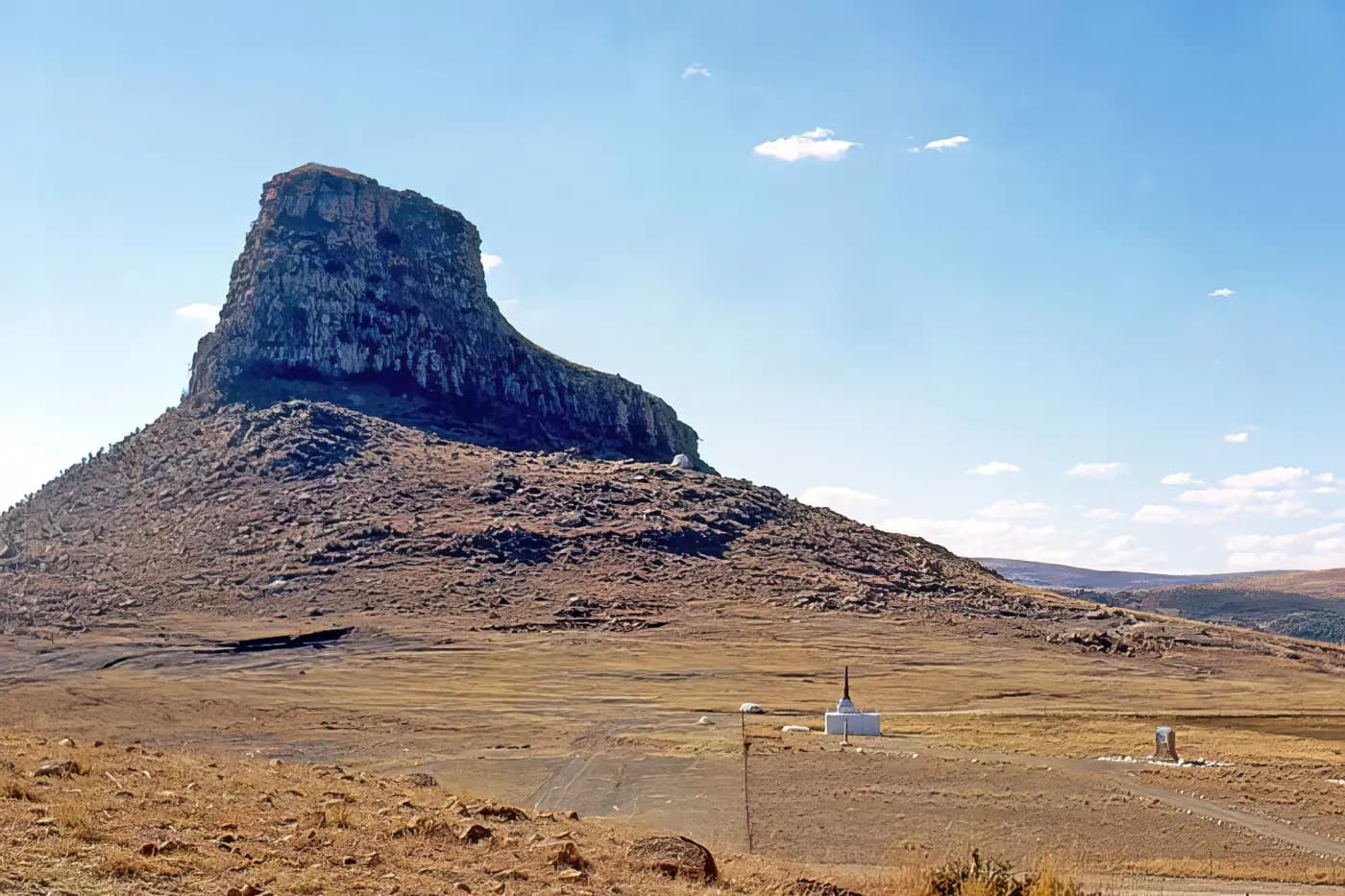 The sphinx-shaped crag of Isandlwana rising above the dry battlefield, with white memorials on the plain below