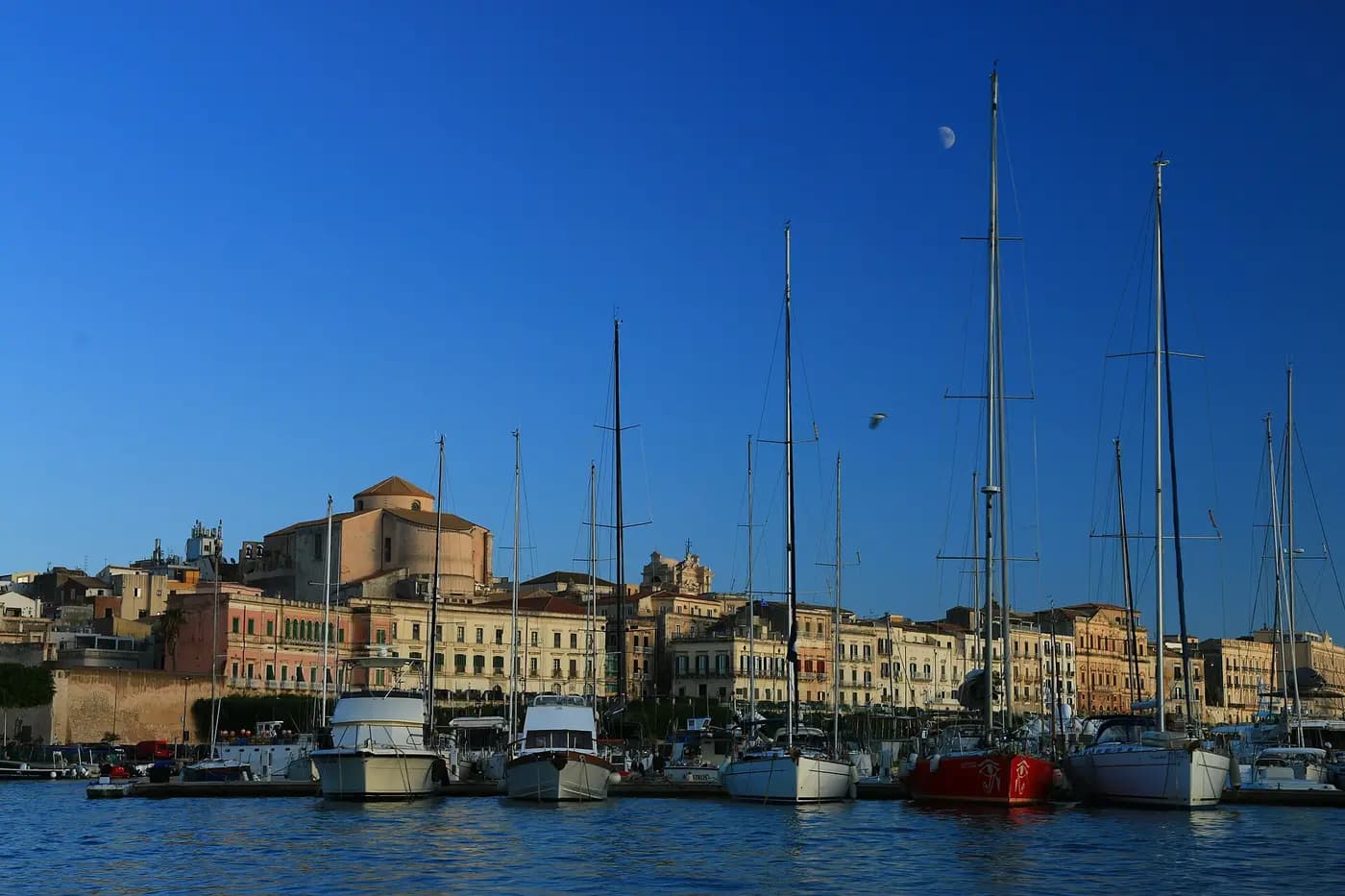 The old island town of Ortigia in Syracuse, seen across the harbour with sailing boats moored