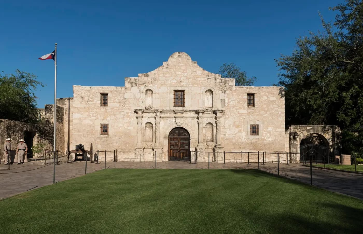 The humped limestone façade of the Alamo mission church in San Antonio, behind a lawn
