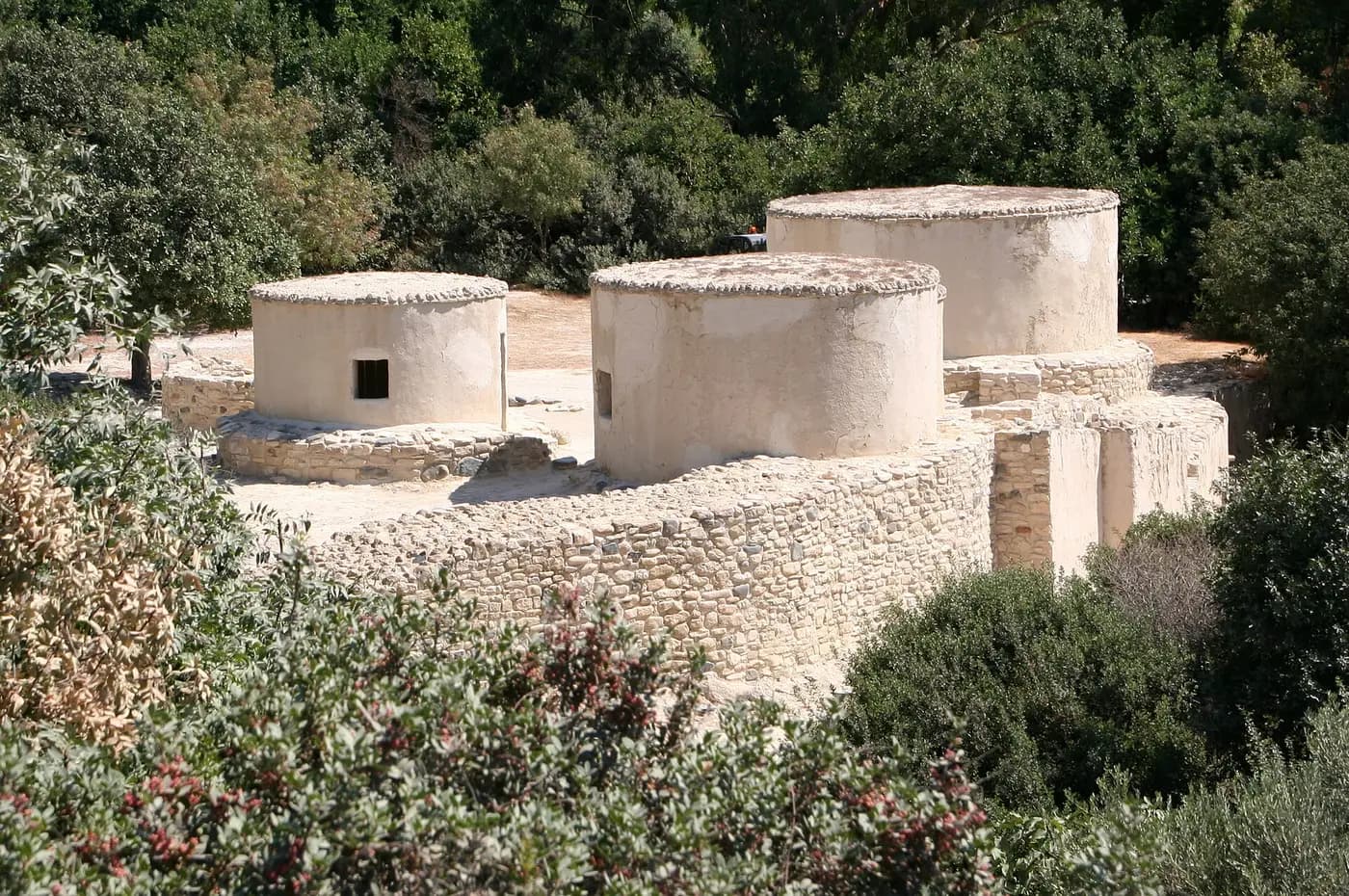 Reconstructed round stone houses with flat roofs at the Neolithic settlement of Choirokoitia, among green shrubs