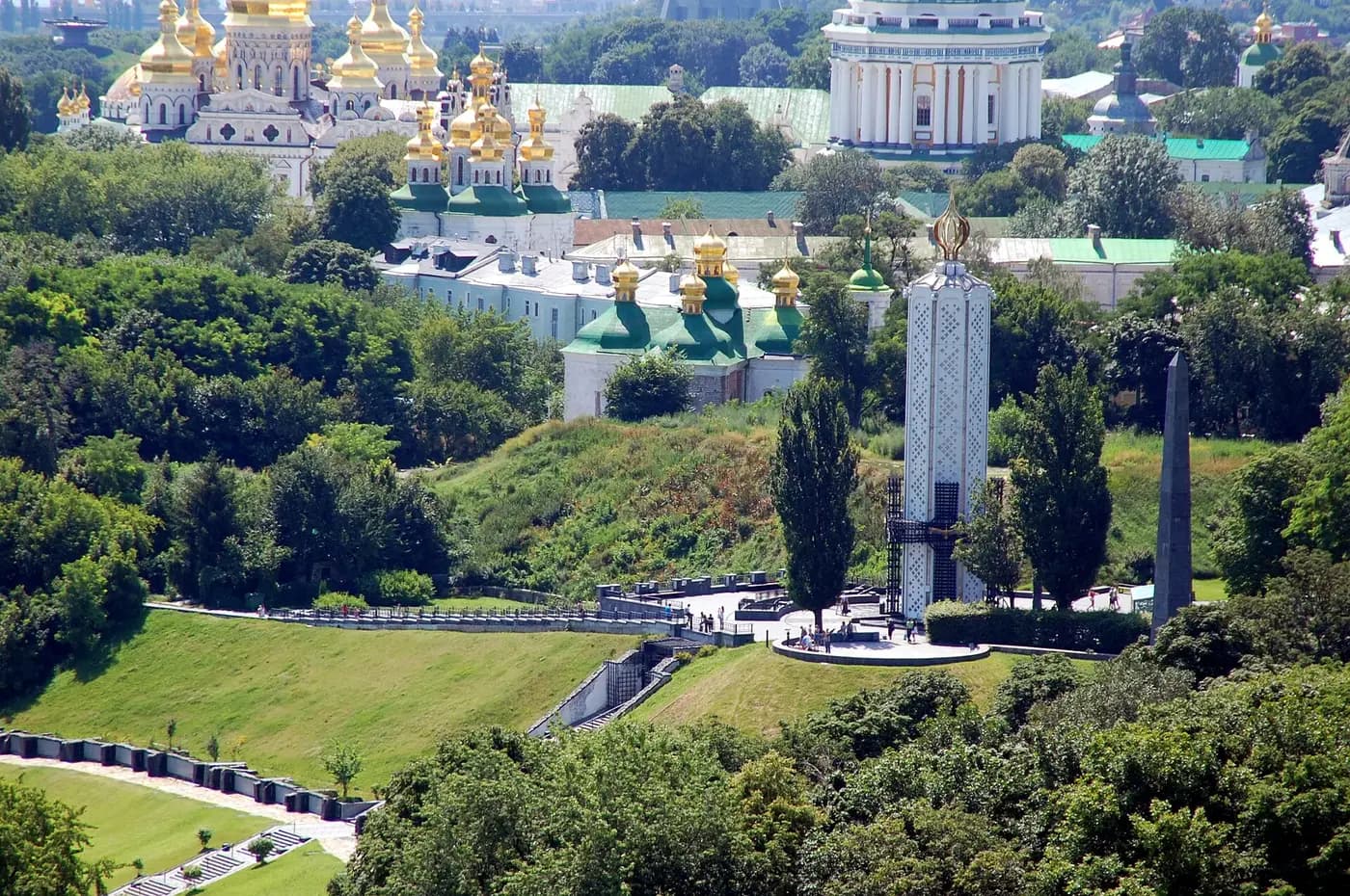 The white Candle of Memory at the Holodomor memorial in Kyiv, with the domes of the Lavra behind