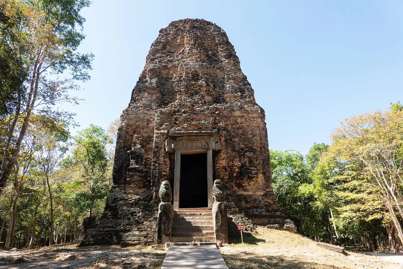 A brick tower sanctuary at Sambor Prei Kuk, with stone lions guarding its doorway, in dry forest