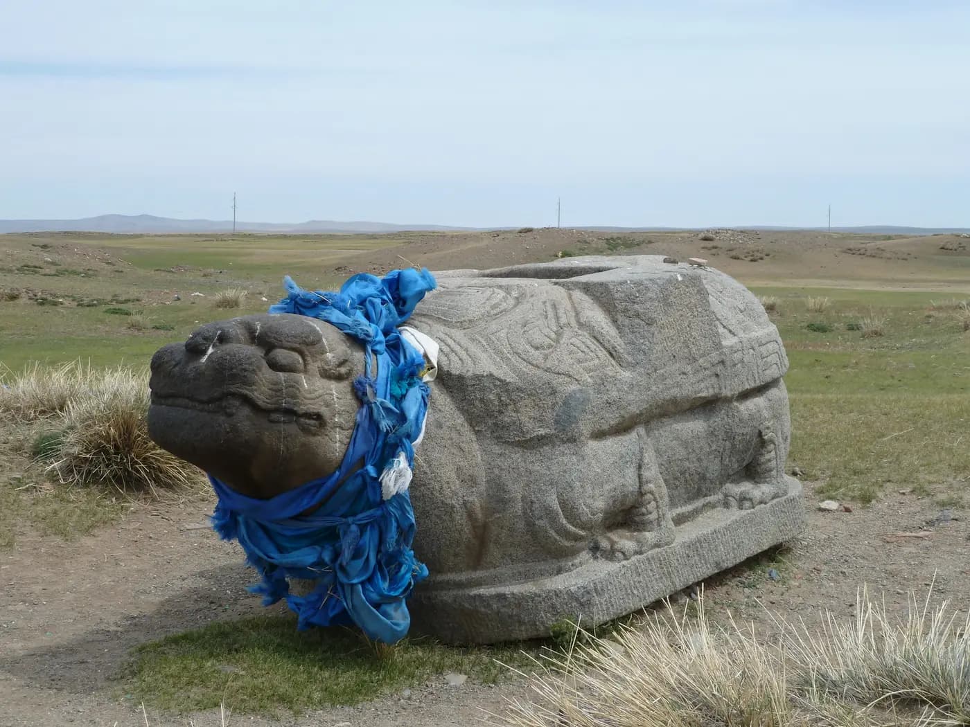 A granite turtle from Karakorum, draped in a blue khadag scarf, on the open steppe at Kharkhorin