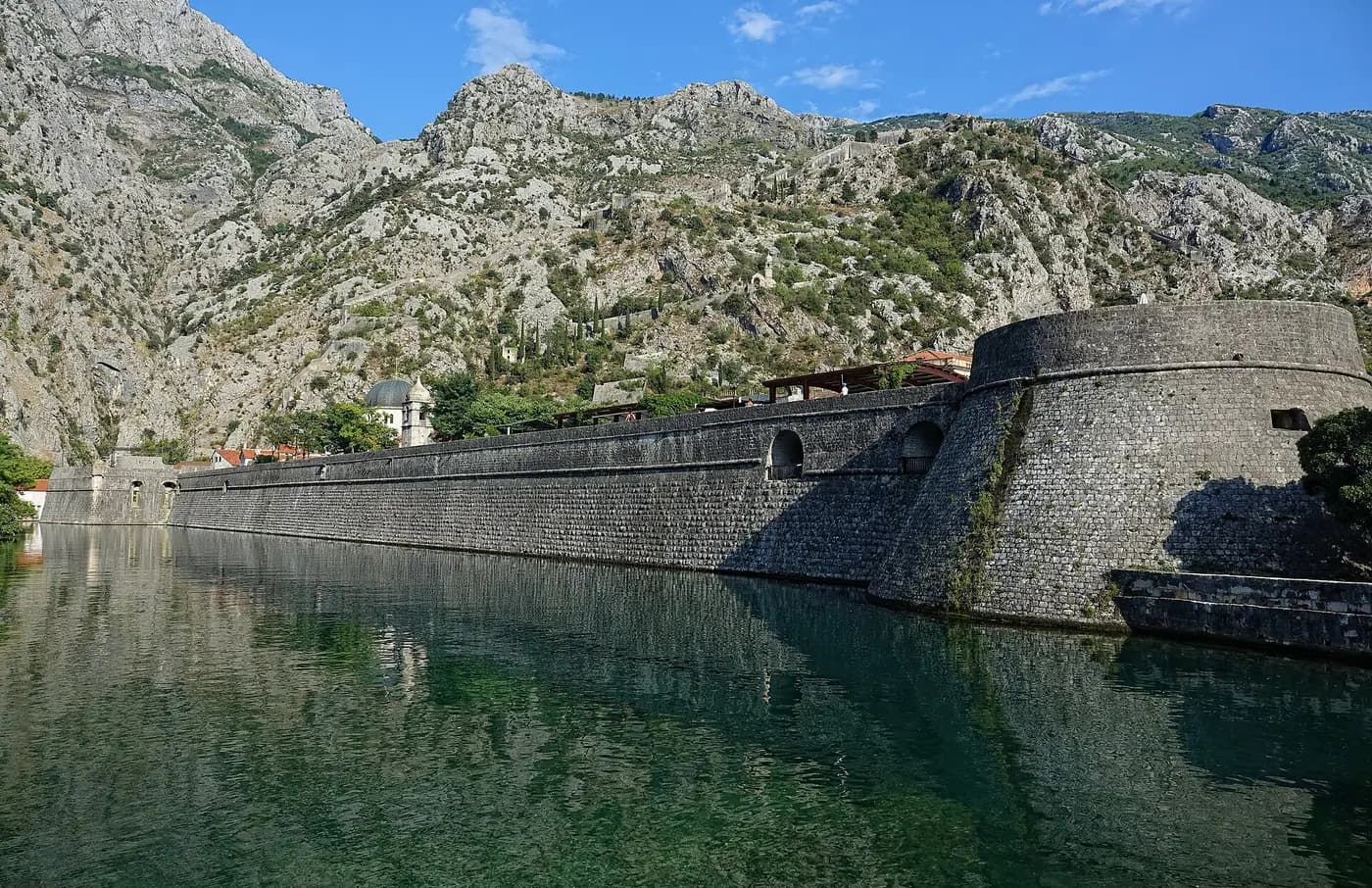 Kotor's Venetian-era walls and a round bastion reflected in the water below steep limestone mountains