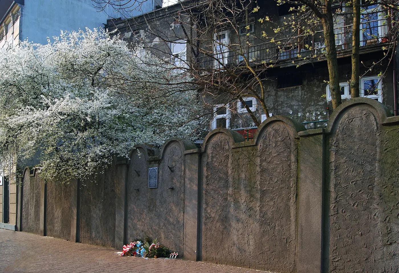 A surviving stretch of the Kraków ghetto wall on Lwowska Street, its top shaped like tombstones, with a plaque