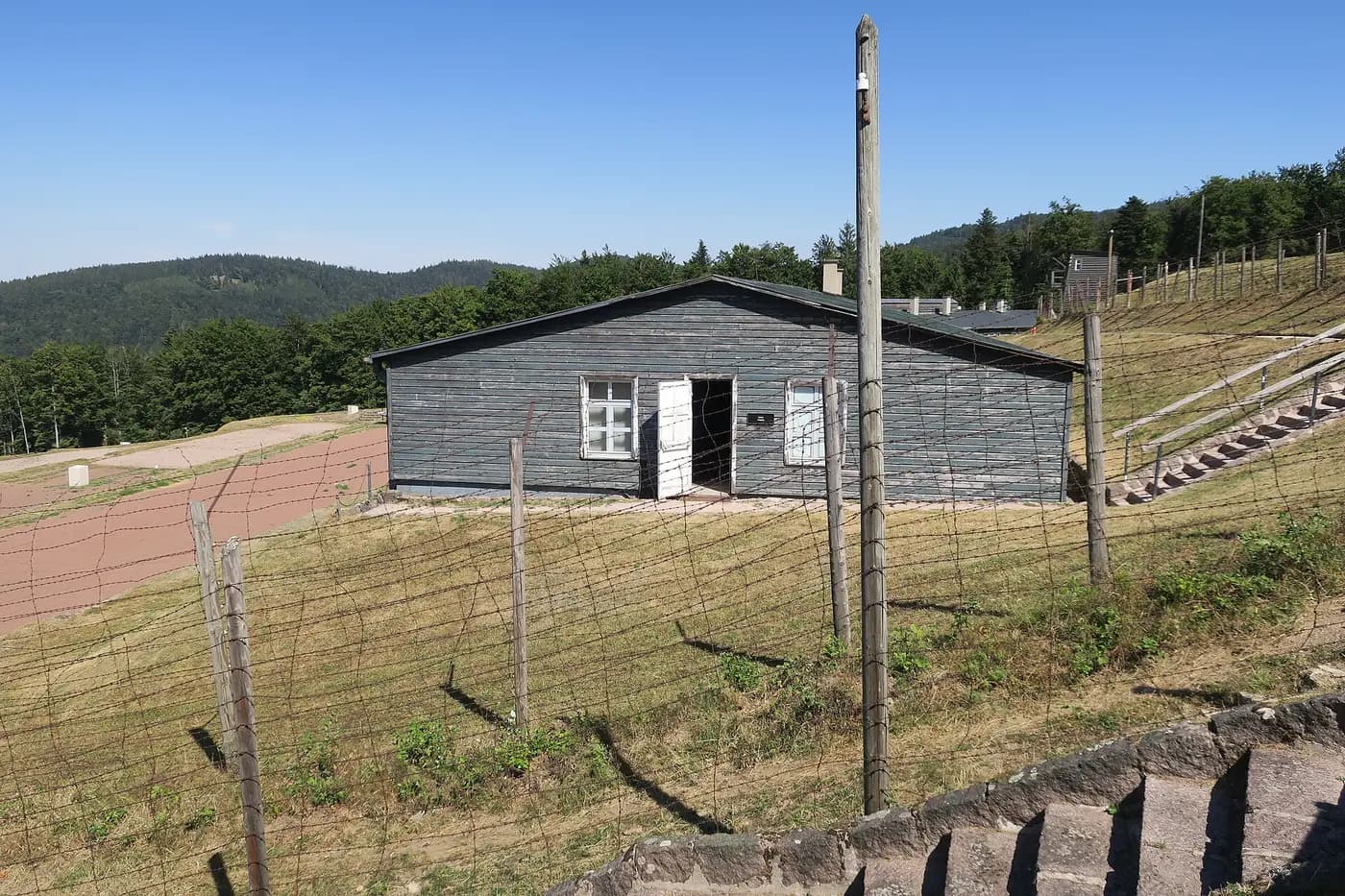 A wooden barrack behind barbed-wire fencing on the terraced hillside of the former Natzweiler-Struthof camp