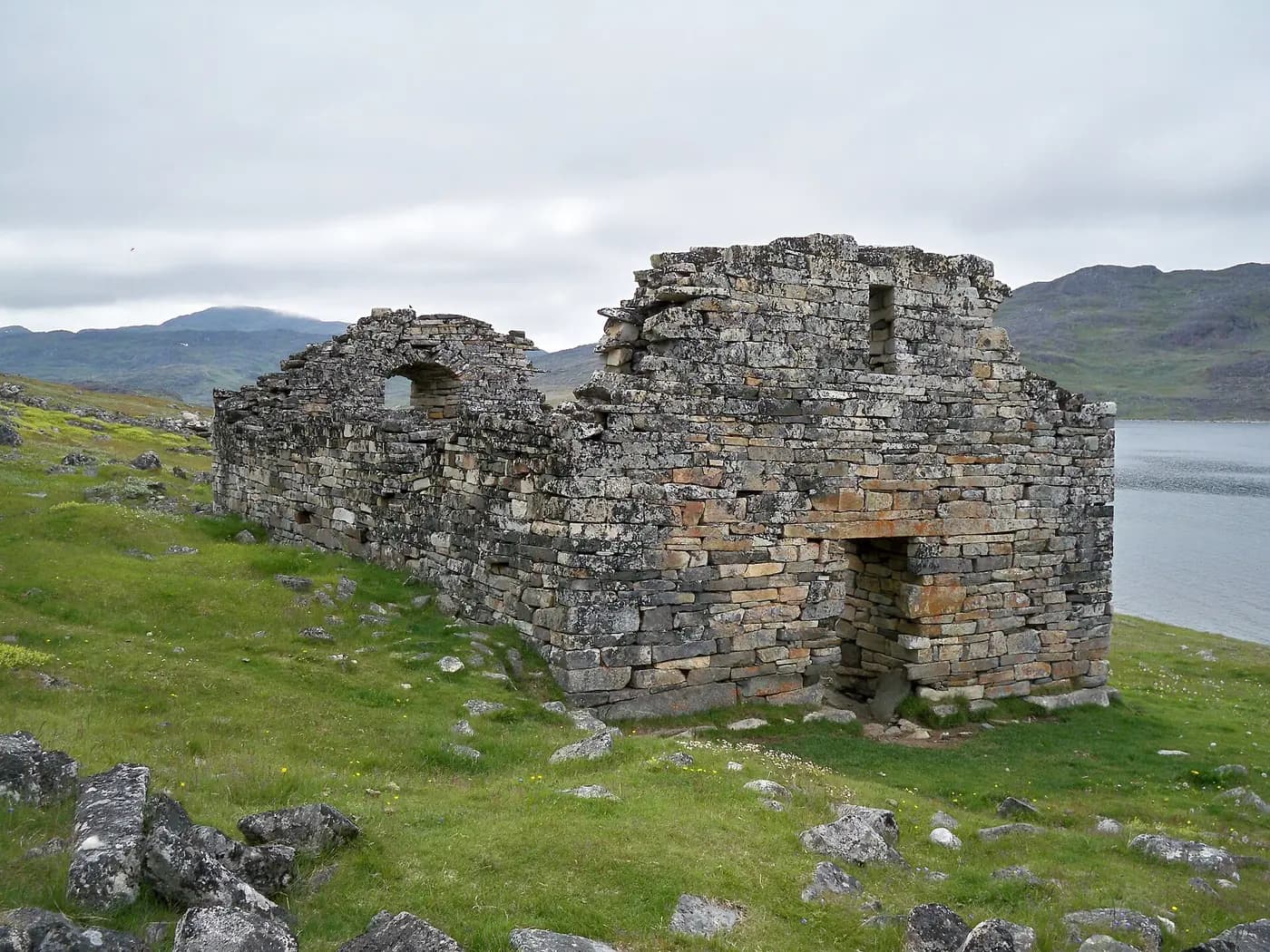 The roofless stone ruin of Hvalsey church on a grassy slope beside a Greenland fjord