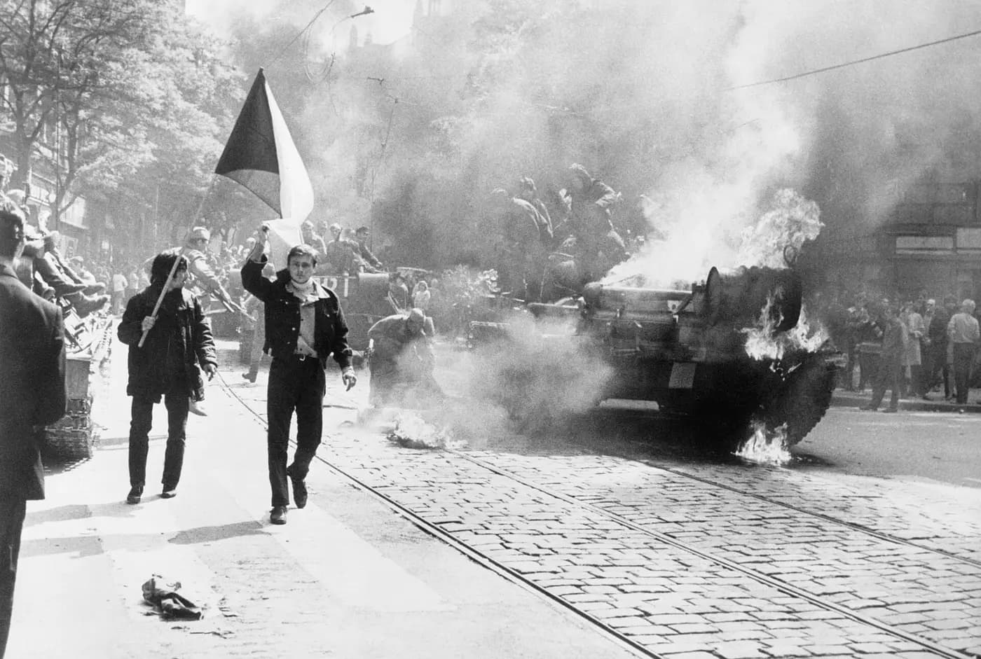 Czechoslovaks carry their national flag past a burning tank in Prague during the August 1968 invasion