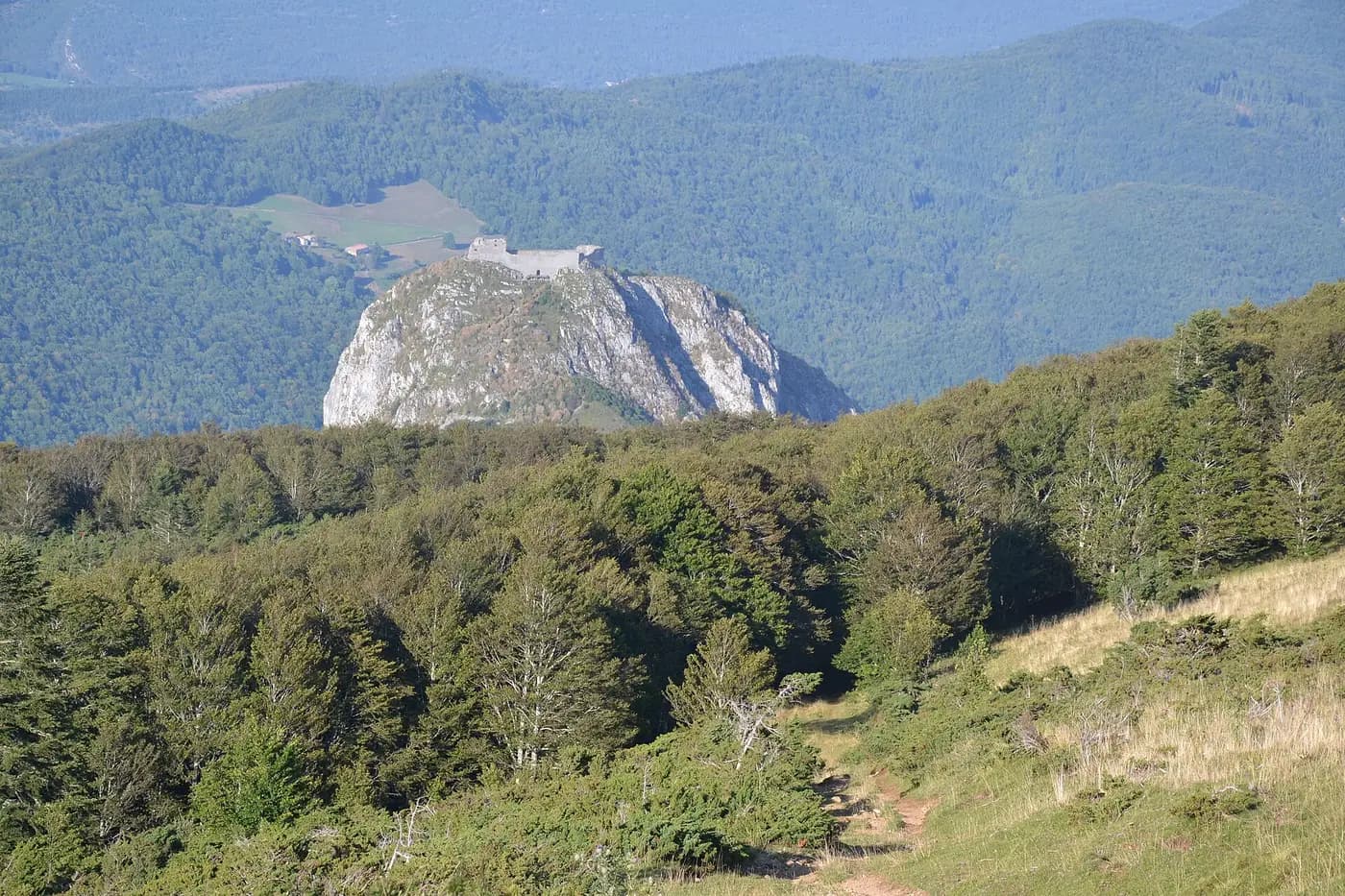 The ruined castle of Montségur on its steep rocky peak above wooded Pyrenean slopes
