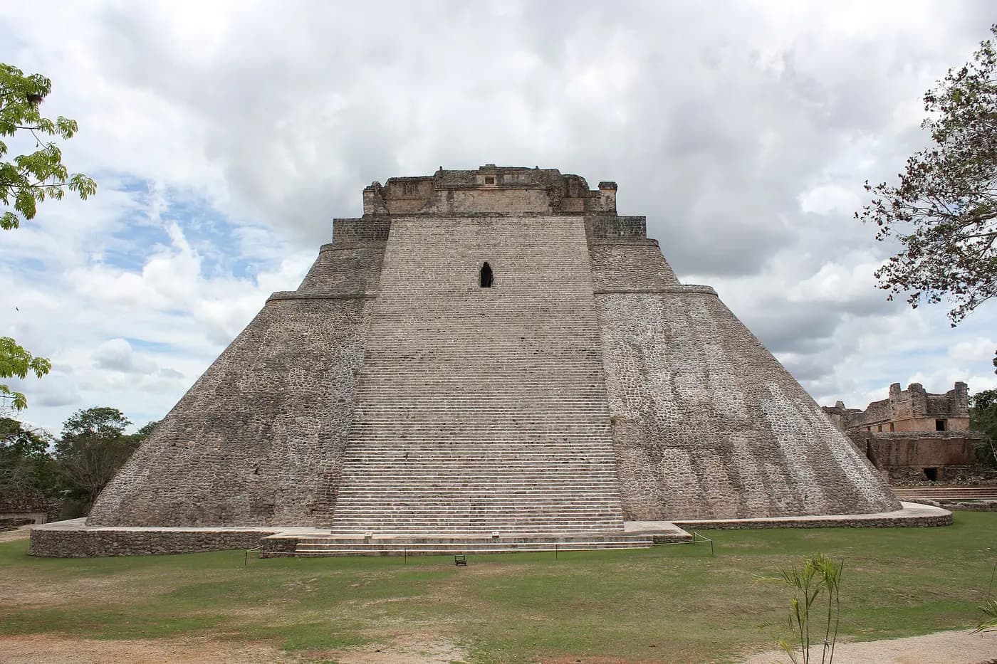 The steep, rounded Pyramid of the Magician at Uxmal under a cloudy sky