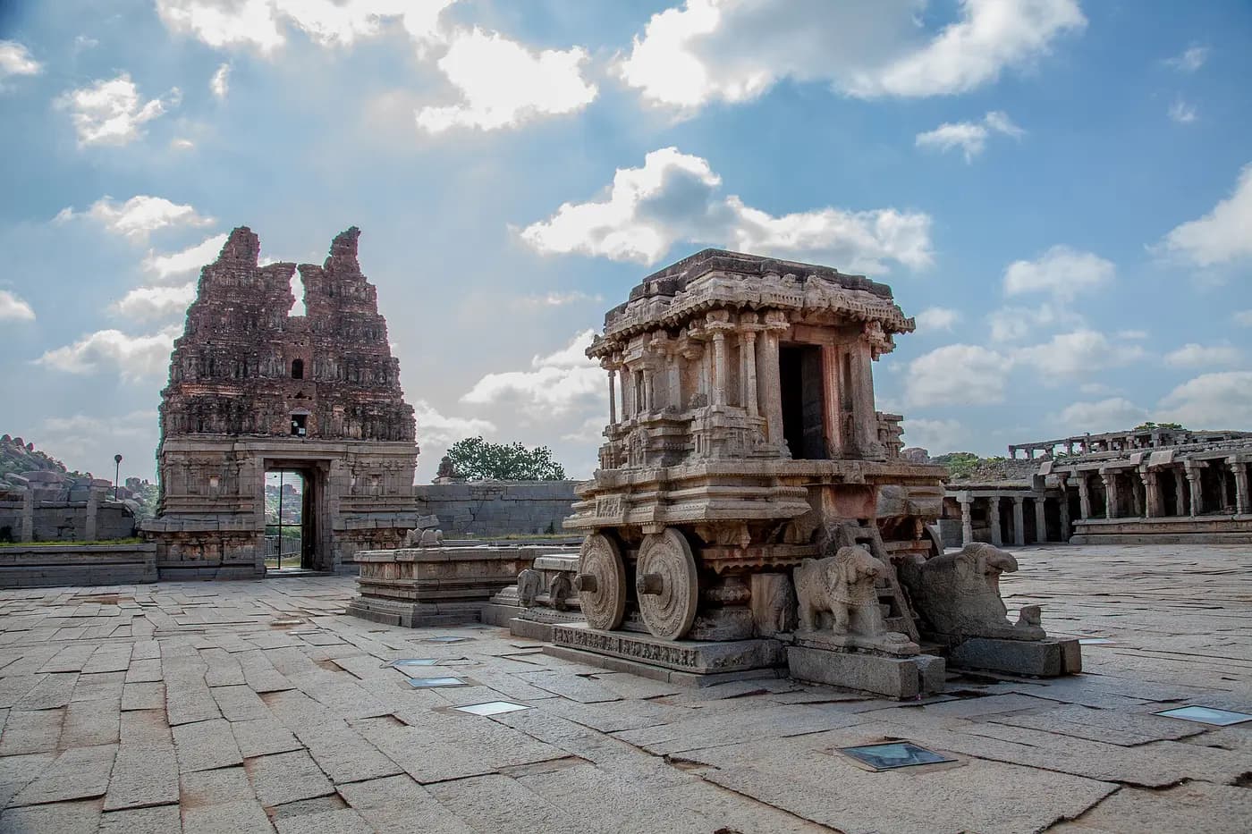 The carved granite stone chariot in the Vittala Temple courtyard at Hampi, with the ruined gateway behind