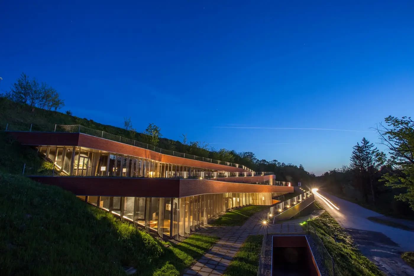 The terraced Vučedol Culture Museum lit up at dusk, built into a grassy hillside