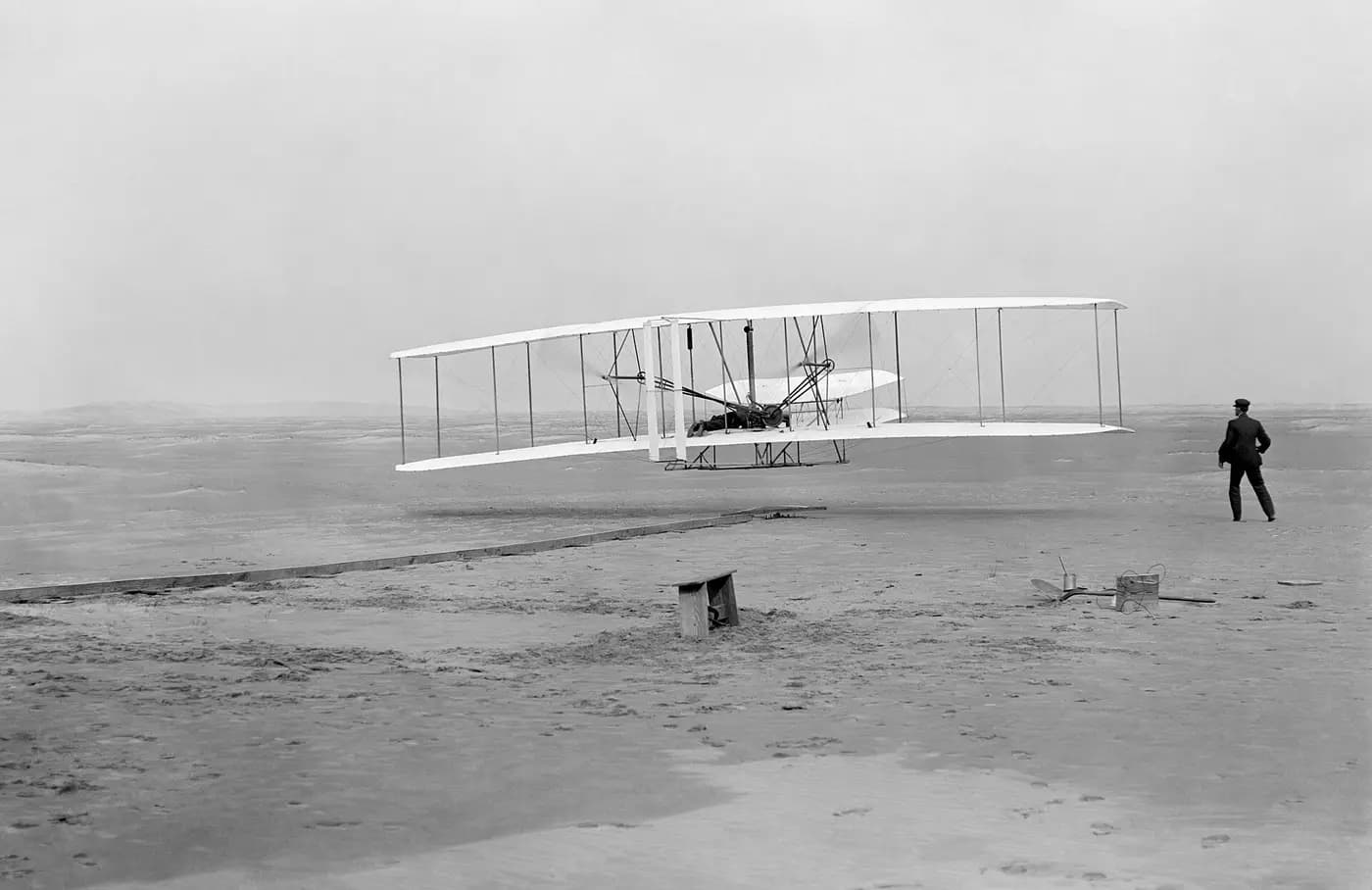 The Wright Flyer lifting off at Kill Devil Hills on 17 December 1903, Wilbur running beside it