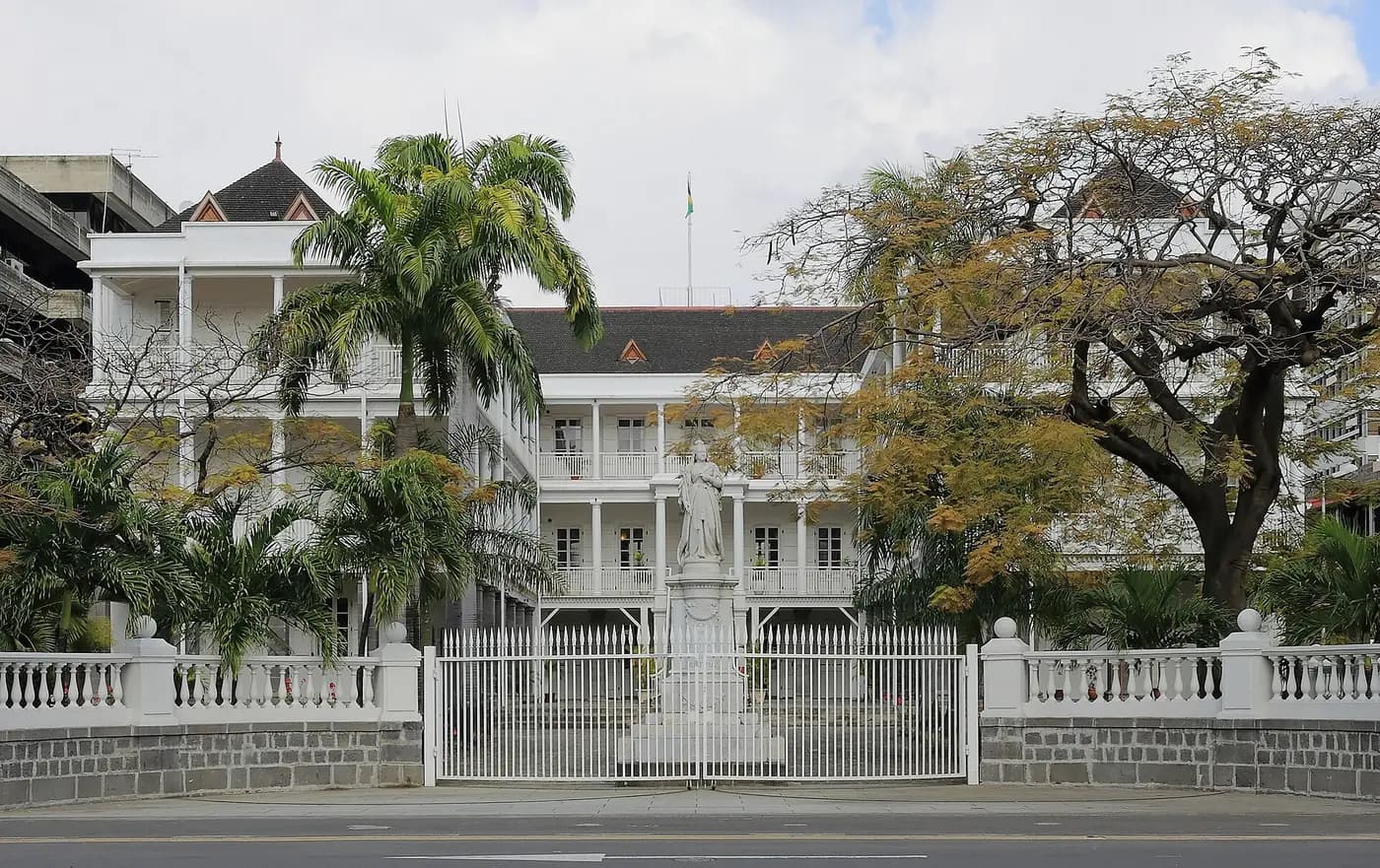 The white colonial Government House in Port Louis, seen past palm trees and a statue at its gates
