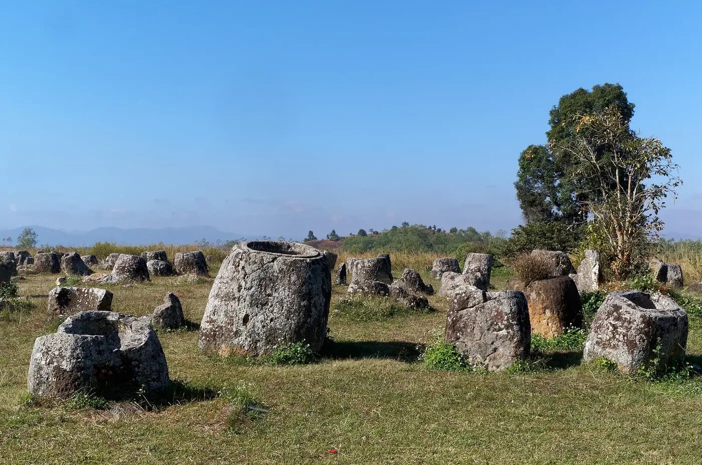 Large carved stone jars scattered across the grassland of Plain of Jars Site 1 in Laos