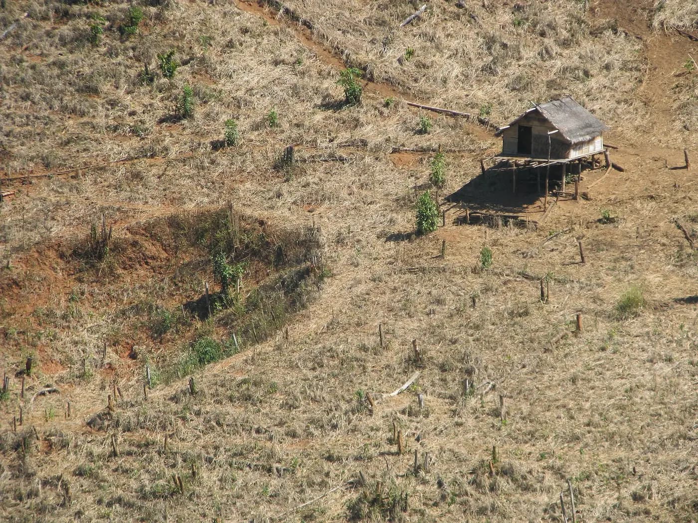 A bomb crater in a cleared Lao hillside field beside a stilt hut, a legacy of the 1964–73 bombing